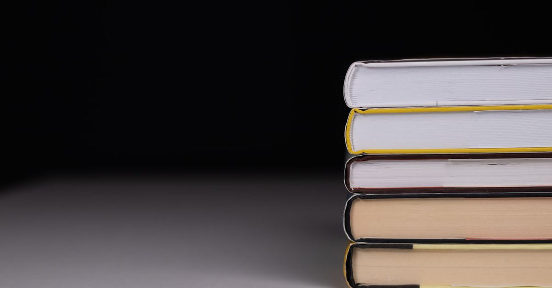 A stack of books on fertility and conception on a wooden table, with a cup of tea and a notebook, in soft natural light.