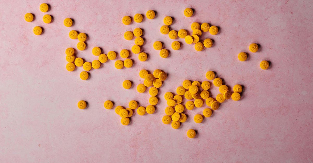 A small glass bottle of vitamin B12 sublingual tablets next to a single peach-flavoured lozenge on a clean white surface, illustrating a vit b 12 sublingual supplement.