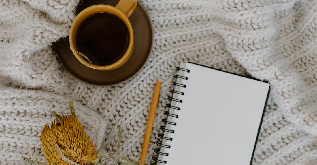 A menopause self care guide book resting on a soft blanket beside a cup of herbal tea and a lit candle, creating a calming self-care moment.
